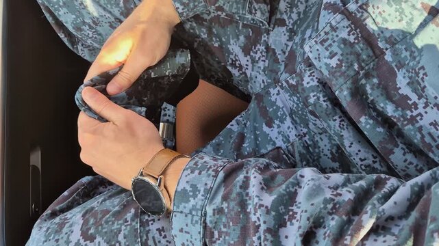 A soldier in camouflage uniform nervously clutches his cap, close-up
