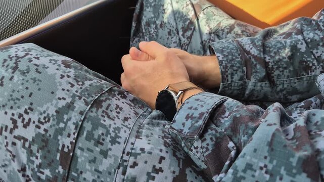 A soldier in camouflage uniform nervously fidgets with his fingers, close-up