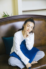 Fototapeta premium Relaxed young woman sitting on sofa with blue cushion at home