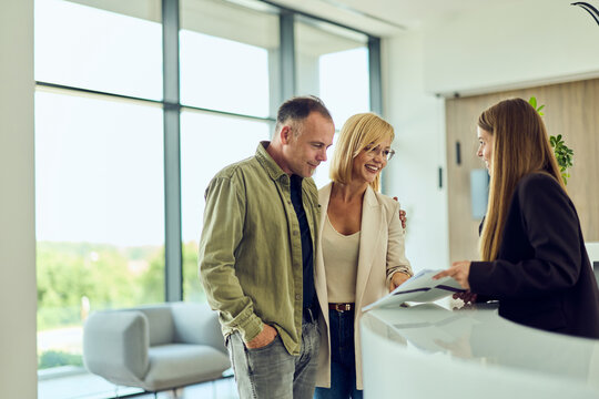 Couple Checking In At Modern Hotel Reception With Friendly Receptionist And Warm Service