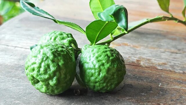 Fresh green kaffir lime fruits on branch over wooden background.