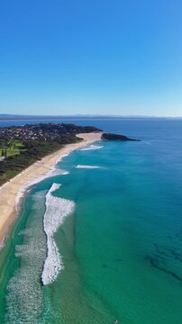Aerial vertical video panning around One Mile Beach near Forster, NSW, Australia. The sweeping camera movement showcases the expansive sandy shoreline, rolling Pacific Ocean waves and coast