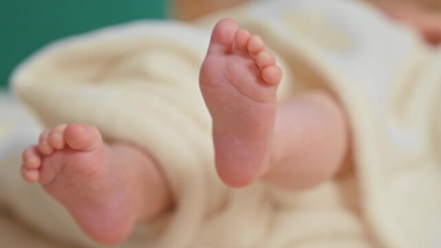 Baby girl feet with curled toes gripping a soft cream blanket, legs bent and feet touching in studio; new life tenderness.