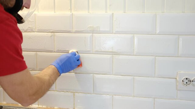 Thoroughly cleaning the grout between tiles. Manually cleaning stains on white tiles. Close-up of a gloved hand cleaning white tiles. A variety of tile cleaning products. The problem of cleaning.