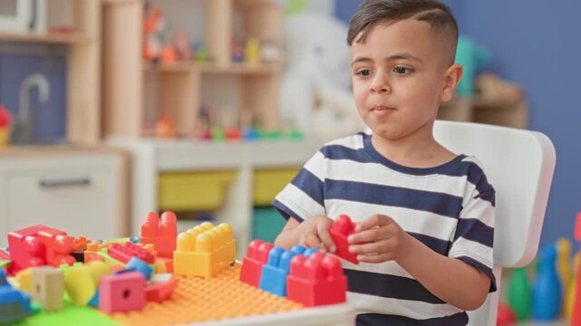 Little boy stacking colorful plastic blocks on a preschool classroom table with focused hands; quiet concentration.