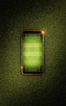 Mobile phone with soccer field screen on green grass lawn, top view