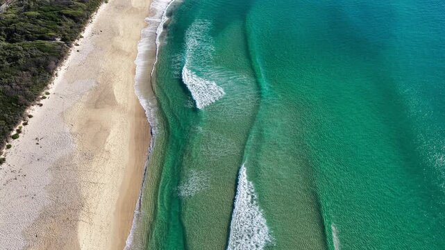 Aerial video beginning with a downward view before panning up to reveal One Mile Beach, Bennetts Headland and the residential areas of Forster, NSW, Australia.
