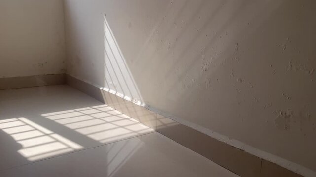 Sunlight casting sharp diagonal striped shadows on an indoor dampness moldy patches painted wall