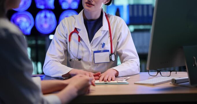 Doctor with stethoscope consults woman as sits at desk with computer. Female patient listens to physician recommendation at appointment in hospital