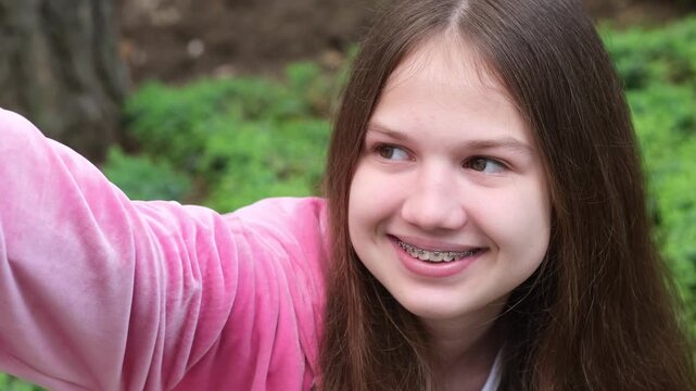 Smiling teen girl with dental braces taking a selfie outdoors. Teeth health care, orthodontic concept