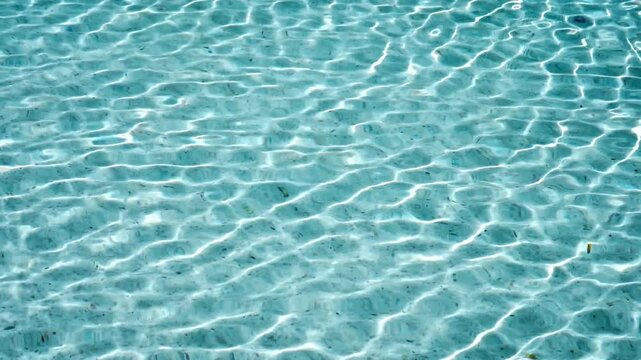 Clear blue water surface with ripples and sunlight reflection in swimming pool.