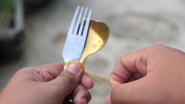 A spoon and fork bound by a yellow rubber band on black.