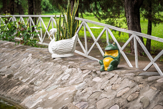 Detalles ornamentales de un sapo y un sisne junto al estanque del cementerio de Jujuy en entorno verde y apacible