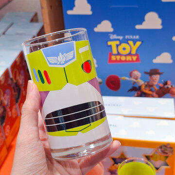 Close up of hand holding a glass tumbler printed with Disney Pixar Toy Story Buzz Lightyear space ranger suit design in front of its official retail product box on June 10, 2026 in Bangkok, Thailand