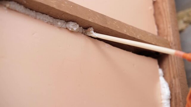 Applying thermal insulation foam with a gun. Using polyurethane foam along wall joints. Expanding the material. Sealing joints and soundproofing walls. Interior renovation. Close-up. Copy space.
