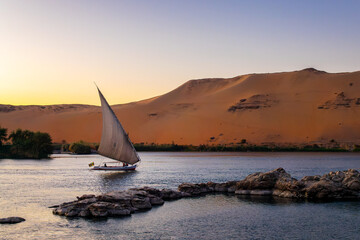 Sand dune and Felucca (traditinal egyptian sailing boat) on the Nile river at sunset  in Aswan, Egypt © Delphotostock