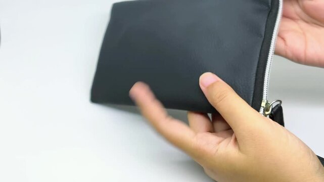 Persons Hands Opening and Closing a Black Textured Zipper Pouch on a White Background
