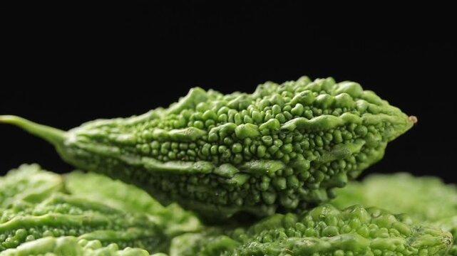 Pile of fresh bitter melons slowly rotating on a black background. Close-up view