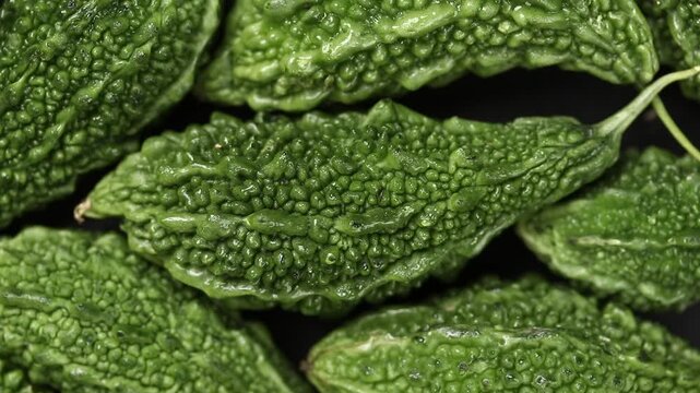 Pile of fresh bitter melons slowly rotating on a black background. Top view shot
