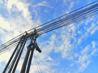 Fototapeta premium Utility poles with tangled electrical wires and cables against a blue cloudy sky