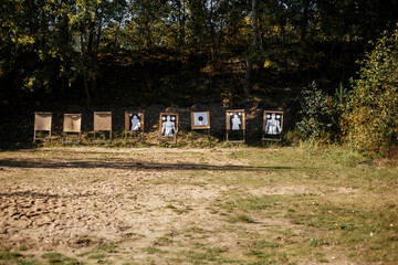 Outdoor shooting range with multiple targets lined up against a dense woodland backdrop. The scene shows a structured training area in a natural forest environment © Olga Yashnikova