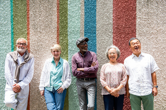Diverse group of smiling seniors standing against a colorful wall.
