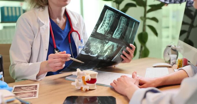 Doctor woman holds spine x-ray images and talks to patient in clinic. Medical professional analyzes helps with injury recovery to female in hospital