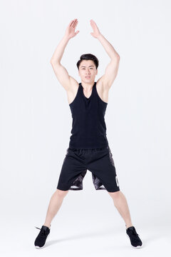 Young athletic man doing jumping jack exercise in studio