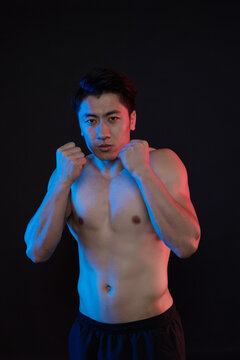 Athletic shirtless man in fighting stance with dramatic blue and red lighting