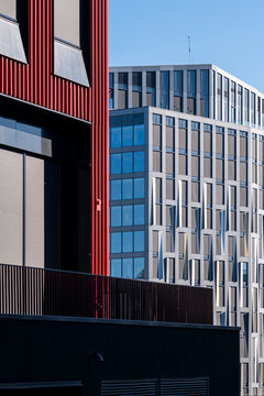 Red facade edge and blue windows frame an urban building, with vertical architecture, geometry, contrast, exterior shadow, and layered city depth