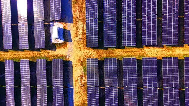 Overhead solar modules at crossroads of service paths. Aerial view of blue photovoltaic panels around an earth-tone intersection with a small white structure.