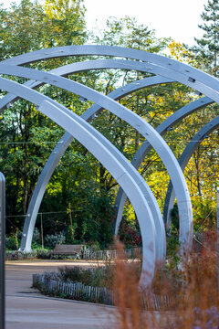 White arches curve through an urban garden, where planting, pathway, trees, landscape structure, and exterior design create a sculptural public space