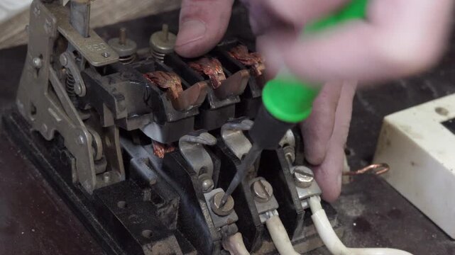 Electrical equipment maintenance, Electrician's hands repairing an old industrial three-phase automatic circuit breaker using a screwdriver, close-up