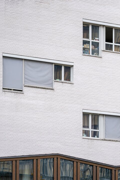 On the white brick facade, small windows and shutters keep the urban building exterior quiet while architecture, texture, and geometry do the work