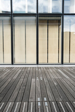 The wooden deck leads to a glass facade, making the urban terrace feel like architecture as windows hold reflection and perspective in long lines