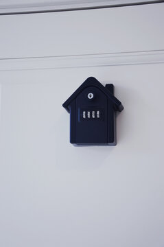 A wall mounted black key lock box with a combination lock mounted above a traditional keyhole on a white door