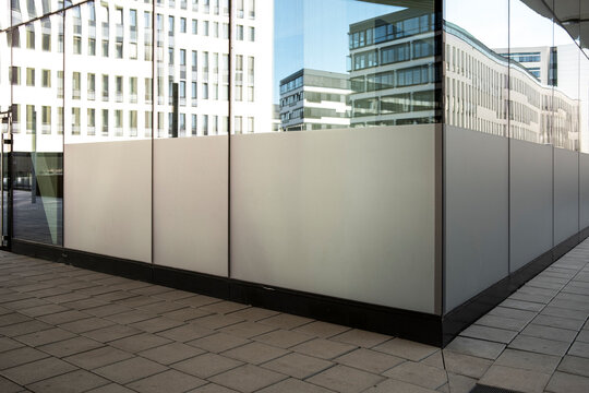 A glass reflection wraps the terrace corner, where the urban building facade turns plaza windows and pavement into a calm mirrored edge