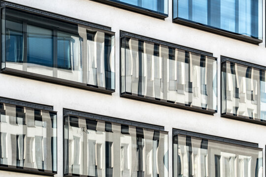 Behind rows of white curtains, windows and glass reflection soften the urban building facade, letting daylight slide across a quiet exterior grid