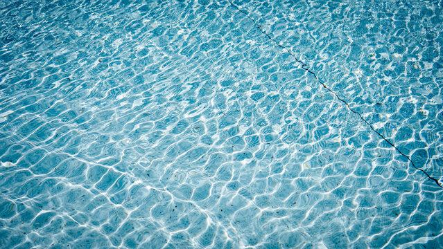 Clear blue swimming pool water surface with ripples and sunlight reflection.