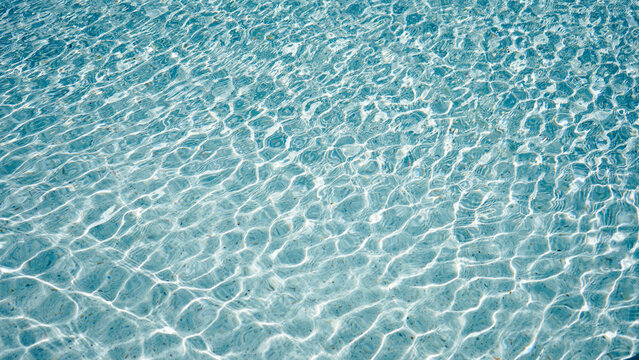 Clear light blue swimming pool water surface with ripples and sunlight reflection.