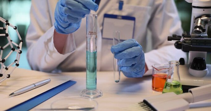 Woman scientist takes blue liquid with pipette from beaker in chemical lab. Female technician tests reagent color substance in medical research center