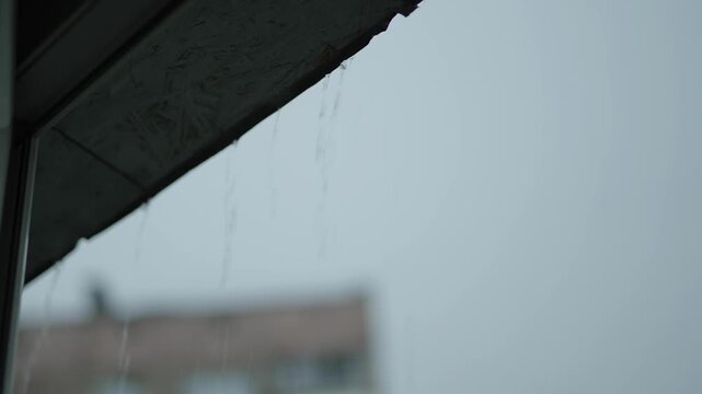 Water dripping from a wooden roof edge against cloudy sky