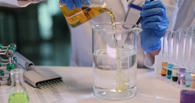 Female assistant pours oil into water and stirs in chemical lab. Woman technician researches combination of different substances in laboratory