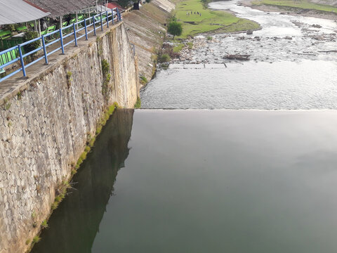 A water reservoir next to a dam structure with a retaining wall and river channel surrounded by natural scenery. This image highlights the water management infrastructure and flood control system.