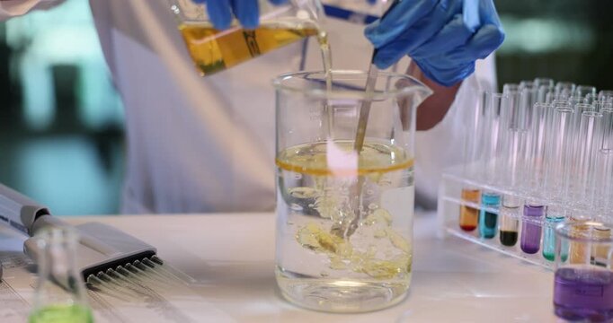 Woman chemist stirs oil and water in large beaker in research lab. Scientist in gloves analyzes reaction of fluids in agricultural center slow motion