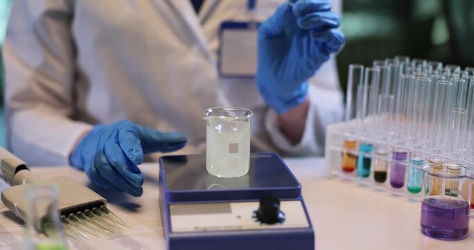 Female chemist uses vibrator to stir oil and water in research lab. Woman technician in gloves turns on device to process substance in laboratory