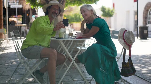 Senior man and woman tourist take a selfies while at a cafe with coffee near the historic Loreto mission church in Baja California Sur, Mexico, enjoying their time together.