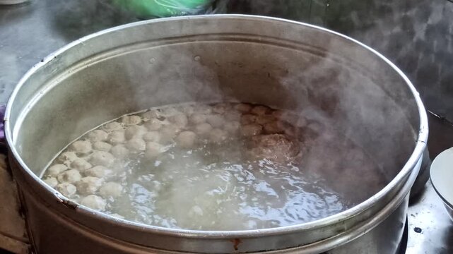Large cooking pot filled with steaming meatball soup and assorted meatballs, showcasing authentic Indonesian culinary tradition.