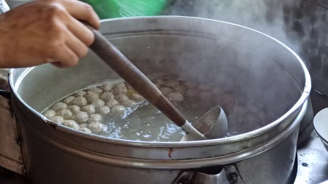 Large cooking pot filled with steaming meatball soup and assorted meatballs, showcasing authentic Indonesian culinary tradition.