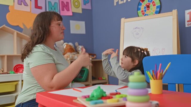 Woman high fives girl with raised hands over crayons and paper in school building; learning bond joy.